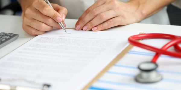 This is an image of a person filling out a form with a stethoscope next to the form.